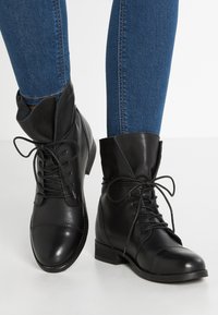 Black leather ankle boots with a rounded toe, lace-up front, and soft fold-over cuff; flat heel and smooth texture.