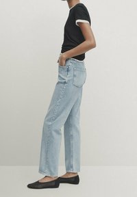 T-shirt nera con polsini bianchi, jeans straight-leg azzurri chiari e ballerine nere. I jeans presentano una tasca posteriore e una vestibilità rilassata.