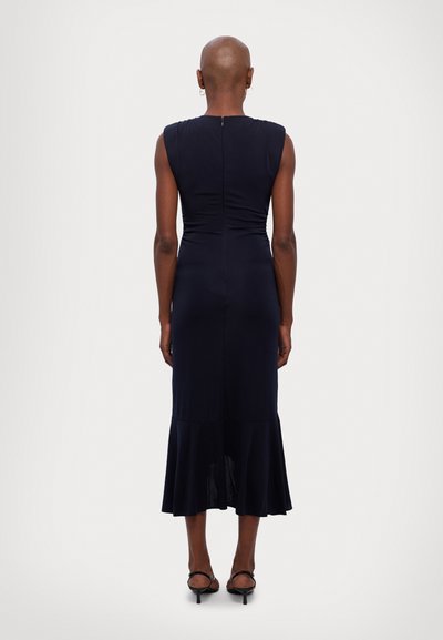 Navy blue fitted dress with cap sleeves and ruching at the waist, featuring a flared hem. Styled with open-toed heels.