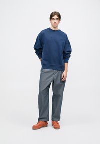 Navy oversized Sweatshirt, graue weit geschnittene Hose und orangefarbene Mokassins. Baumwollmaterial mit gerippten Bündchen und einem dezenten Logodetail.