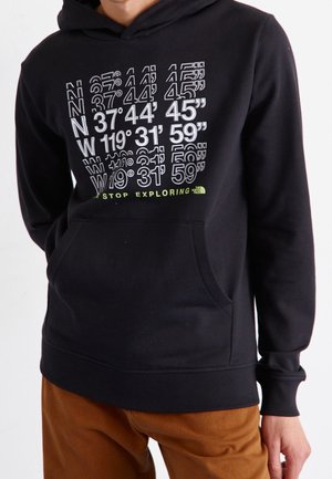 Person trägt einen schwarzen Hoodie mit weißen Koordinaten und dem Text "Never Stop Exploring" über einer Fronttasche.