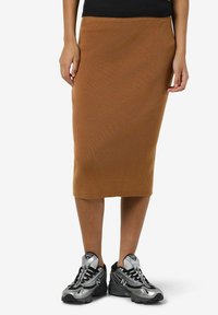 Jupe midi côtelée marron avec une silhouette ajustée, associée à des baskets argentées et noires, mettant en avant une texture de matériaux mixtes.