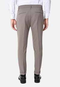 Pantaloni grigi chiari con vestibilità sartoriale, dotati di due tasche posteriori, piega sul davanti e un leggero risvolto alla caviglia. Indossati con scarpe nere.