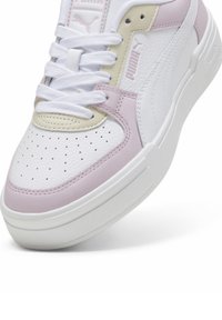 Sneaker in pelle bianca con accenti in rosa chiaro e beige. Presenta una punta perforata, lacci bianchi e una suola in gomma con dettagli testurizzati.