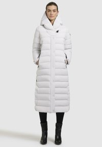 Lang hvid dunjakke med høj krave, knaplukning, vandret quiltning og sidelommer. Båret over sorte leggings og ankelstøvler.