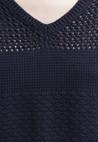 Námořnicky modrý pletený svetr s výstřihem do V a otevřeným vzorem pletení na průkrčníku, s texturovaným designem těla a hladkým zakončením.