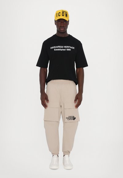 Schwarzes T-Shirt mit weißem Text, beige Cargo-Hosen mit Taschen, weiße Sneaker und eine gelbe Mütze mit schwarzem Schriftzug. Einfaches, modernes Design.