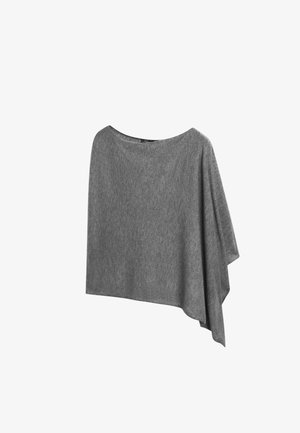 Frau geht, trägt einen grauen asymmetrischen schulterfreien Pullover, weiße Hose mit weitem Bein, weiße Sandalen, hält eine schwarze Clutch.