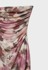 Gros plan sur un tissu froncé avec un motif aquarelle rose, marron, beige et gris sur une partie d’un vêtement.
