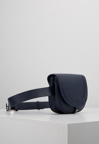 Granatowa skórzana torba na ramię z klapą, regulowanym paskiem i teksturowanym wykończeniem. Z przodu znajduje się srebrny metalowy akcent.