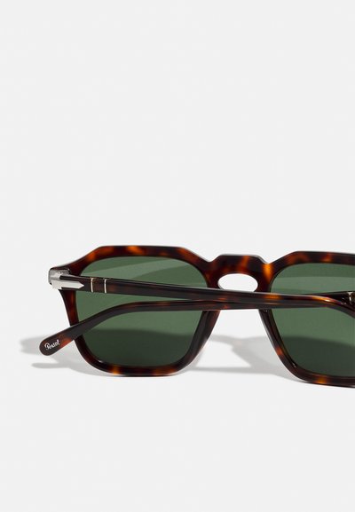 Tortoiseshell sunglasses with green tinted lenses, featuring a prominent hexagonal shape and metal accents on the temples.