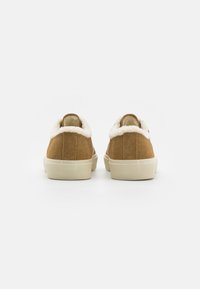 Brown suede sneakers with a white plush lining and beige rubber sole, featuring a rounded toe and minimalist design.
