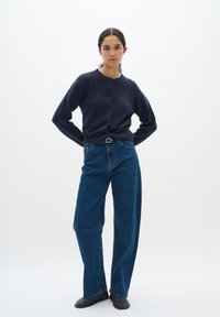 Marinblå stickad cardigan med rund halsringning och fem knappar, kombinerad med hög midja, raka blå jeans och svarta skor.