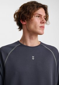 Marineblaue Langarm-Sportshirt aus strukturiertem Stoff, mit kontrastierenden hellen Nähten und einem kleinen silbernen Logo auf der Brust.