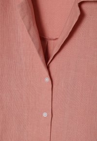 Pink linen shirt with a pointed collar, featuring white buttons and a textured, breathable fabric, highlighting a simple, classic design.