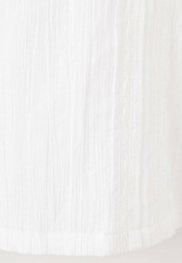 Tessuto di cotone bianco con una superficie testurizzata e screpolata, caratterizzata da sottili linee verticali. Il bordo inferiore è rifinito con una leggera curvatura.