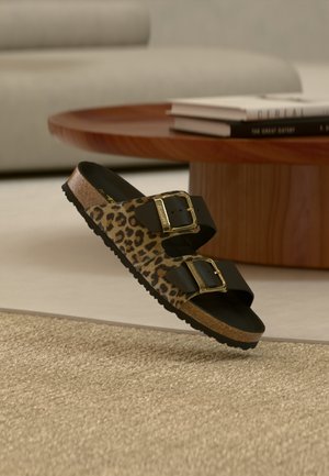 Leopard-print sandals with two black straps and gold buckles, featuring a cork sole and black textured rubber outsole.