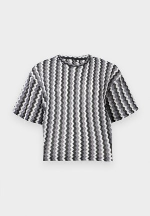 Haut en maille manches courtes avec des rayures verticales en zigzag noir, blanc et gris, avec un col rond, présenté sur un fond uni.