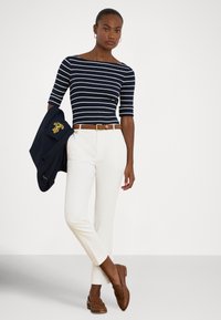 Μπλε σκούρο και λευκό ριγέ μπλουζάκι με λαιμόκοψη τύπου βάρκα, λευκό παντελόνι καλοραμμένο, καφέ ζώνη και καφέ μοκασίνια, σε συνδυασμό με σκούρο σακάκι που κρατιέται στον ώμο.