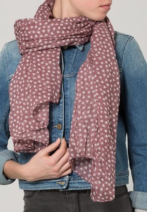 Personne portant une veste en jean tient une écharpe mauve avec des motifs d'étoiles blanches enroulée autour de son cou.