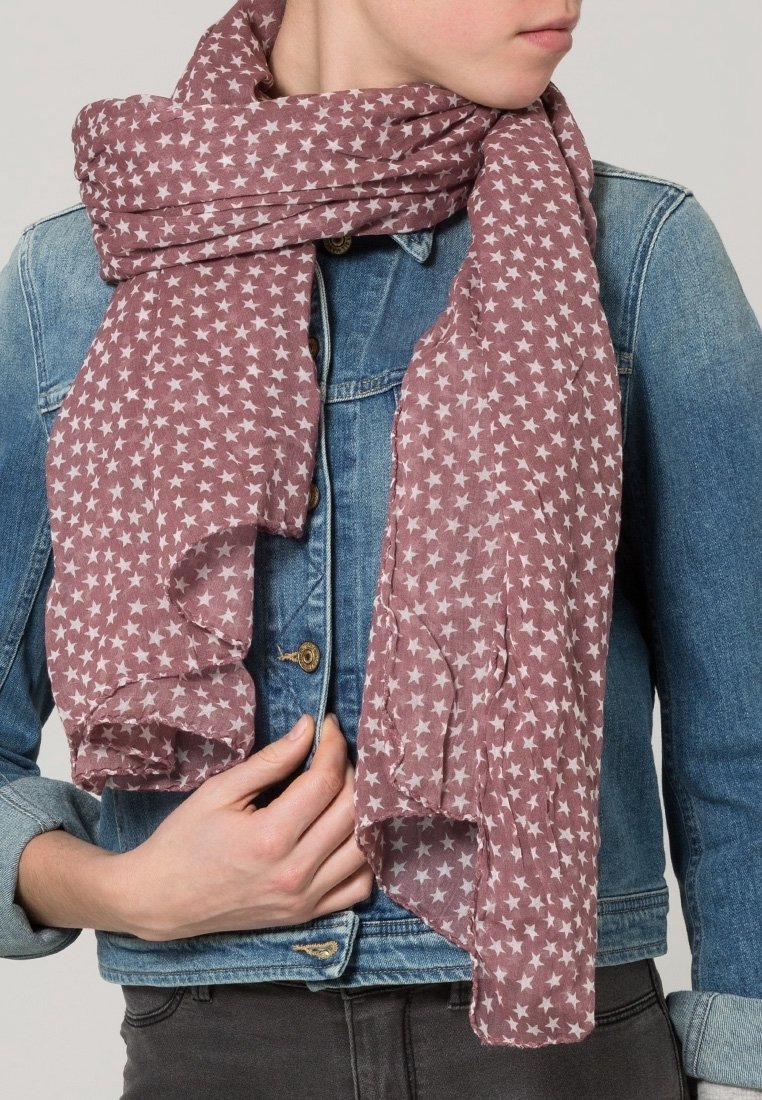 Personne portant une veste en jean tient une écharpe mauve avec des motifs d'étoiles blanches enroulée autour de son cou.