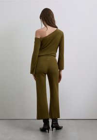 Olive green, ribbed knit two-piece outfit with an off-the-shoulder top and flared pants. Features long sleeves and fitted waistband.