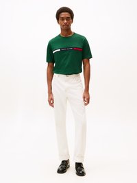 Camiseta de algodón verde con rayas horizontales bordadas en rojo, blanco y azul. Un par de vaqueros blancos remangados y mocasines negros.