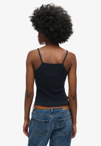 Débardeur en marine �à côtes avec des bretelles fines, design ajusté et finition texturée, associé à un jean taille haute bleu avec une ceinture brune.