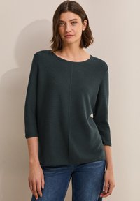 Dunkelgrüner Stricktop mit rundem Ausschnitt, 3/4-Ärmeln und lässigem Schnitt; verfügt über vertikale Nähte und eine glatte Textur.