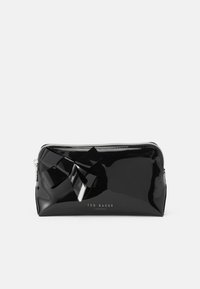 Bolso de charol negro con cierre de cremallera, que presenta un gran lazo decorativo y herrajes plateados, marcado con "Ted Baker London".