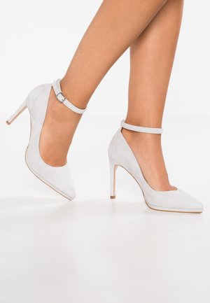 Szare zamszowe buty na wysokim obcasie z wąskim noskiem i paskiem wokół kostki. Obcasy są smukłe i podwyższone, podkreślając elegancki design.