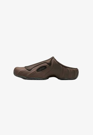Zapato marrón tipo slip-on con un exterior texturizado y moldeado; presenta paneles de malla para transpirabilidad y una forma contorneada para mayor comodidad.