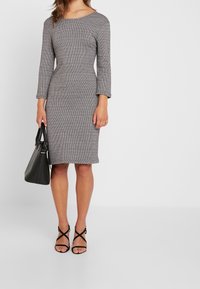 Grå stickad klänning med trekvartslånga ärmar och en figurnära silhuett. Kombinerad med svarta sandaletter med remmar och en svart handväska.