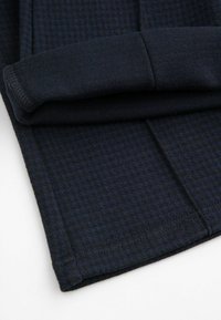 Ciemnoniebieska tkanina w małą kratkę, ukazująca złożony rękaw i szwy dołów na płaskiej powierzchni.