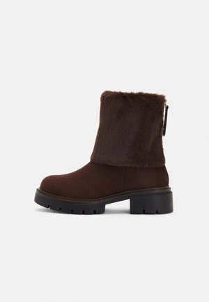 Brown ankle boot with a soft faux fur shaft, block heel, and textured rubber sole. Side zip closure and stitched detail around the base.