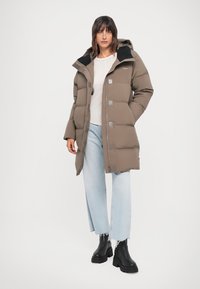 Brown puffer coat with a hood, featuring silver hardware and a quilted design. Paired with light denim and black ankle boots.