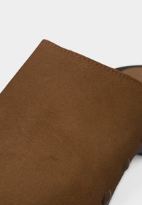 Tige de chaussure en daim marron avec coutures visibles le long du bord supérieur et rivets métalliques sur le côté.