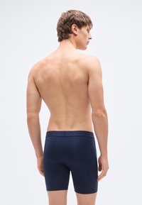 Μπλε ναυτικό boxer briefs με υφασμάτινη μέση που διαθέτει λεπτομέρειες λογότυπου. Το ύφασμα φαίνεται λείο και ελαστικό.