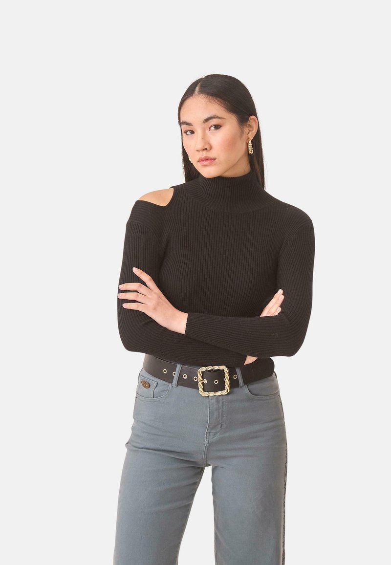 Suéter negro de punto con cuello alto y detalles de corte en los hombros, combinado con jeans gris claro y un cinturón negro con una hebilla decorativa dorada.