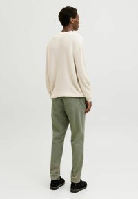 Cream waffle-knit sweater with long sleeves, paired with sage green trousers, and black shoes, viewed from the back against a light background.