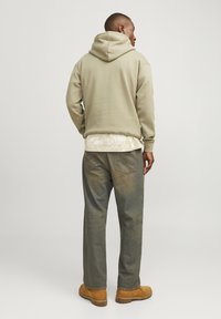 Olijfgroene hoodie met een ontspannen pasvorm. Draag een licht geblokt overhemd eronder, gecombineerd met vervaagde blauwe jeans en tan laarzen.