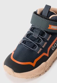 Baskets de sport bleu marine avec des accents orange, tige texturée, lacets élastiques et semelle en caoutchouc étiquetée "STORM". Comprend une bande auto-agrippante.