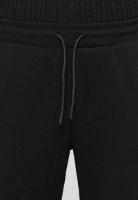 Schwarze Jogginghosen mit einem gerippten elastischen Bund, Kordelzugverschluss, strukturiertem Stoff und seitlichen Taschen. Einfaches Design.