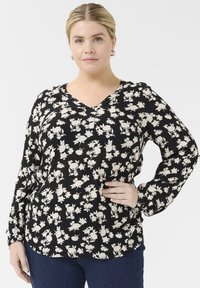 Blusa negra con escote en V, mangas largas y pequeños patrones florales blancos. Está hecha de una tela texturizada con un corte relajado.