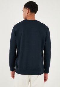 Felpa a maniche lunghe blu navy realizzata in tessuto morbido, con collo a giro e polsini a costine. Texture liscia con dettagli minimali.