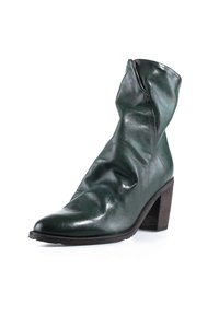 Bottine en cuir vert foncé avec tige souple et talon haut en bois empilé sur fond blanc.