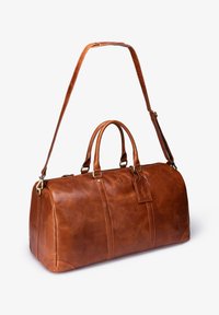Brown leather duffel bag with double handles, adjustable shoulder strap, zipper closure, and a luggage tag. Smooth texture and rounded shape.