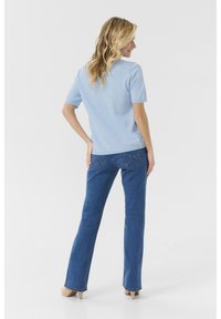 Haut bleu clair à manches courtes avec des pois texturés, assorti à un jean évasé bleu foncé. La tenue est complétée par des talons beiges.