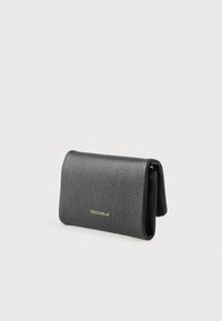 Zwarte leren portemonnee met textuur, voorzien van het gouden COCCINELLE-logo, opvouwbaar ontwerp en zichtbare zijcompartimenten op een lichte effen achtergrond.