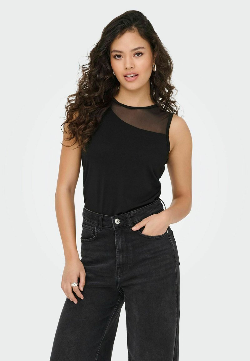 Top noir sans manches avec un panneau transparent sur une épaule, associé à un jean noir taille haute. Texture lisse et design ajusté.